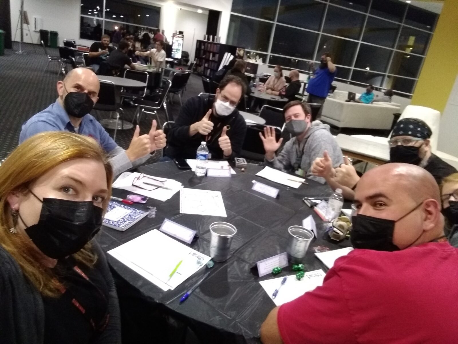 People in face masks gathered around a round table playing TTRPGs.